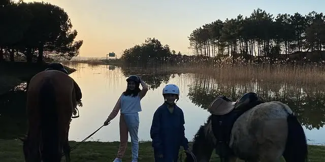 Göl kıyısında gün batımında kasklı çocuklar ve atlar
