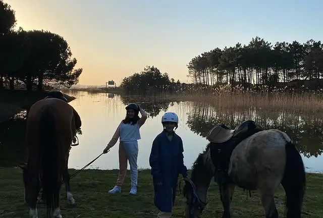 Göl kıyısında gün batımında kasklı çocuklar ve atlar