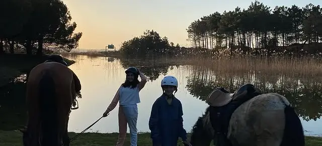 Göl kıyısında gün batımında kasklı çocuklar ve atlar