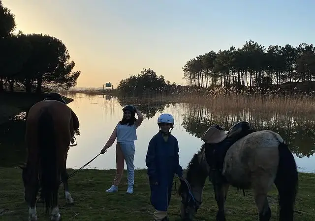 Göl kıyısında gün batımında kasklı çocuklar ve atlar
